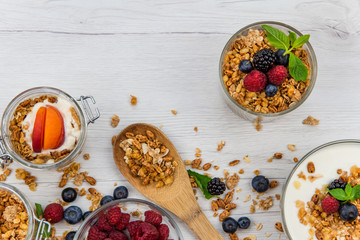 Jars full with granola, yogurt and fresh berries and wood spoon full whit granola on white wood table, top view, selective focus