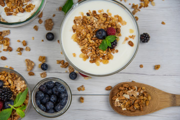 Jars full with granola, yogurt and fresh berries and wood spoon full whit granola on white wood table, top view, selective focus