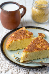Two pieces of homemade pie from millet on a round dish, next a clay mug with milk on an old wooden table. 