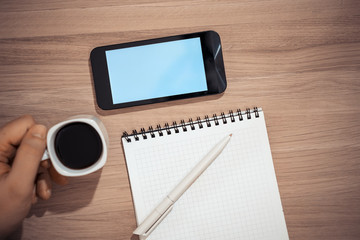 On the table is a smartphone with a blue screen and a laptop with a pen.