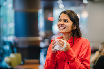 Happy youthful Indian lady smiling and enjoying a coffee in a cafe
