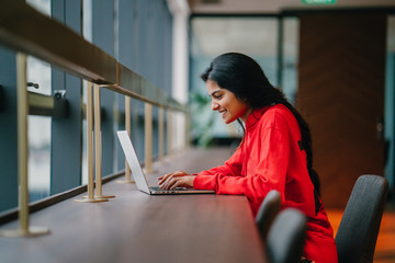 A successful youthful Indian woman smiling and working at a laptop 
