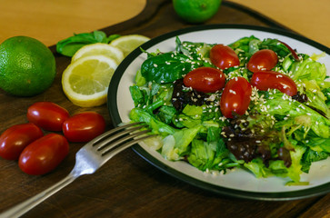 Fresh salad from different kinds of greens and a cherry tomato, dressed with olive oil and sprinkled with sesame seeds