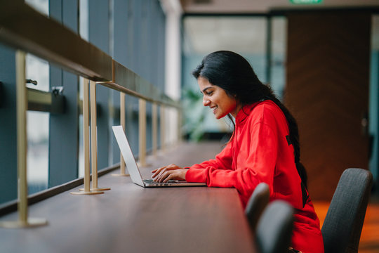 A Successful Youthful Indian Woman Smiling And Working At A Laptop 