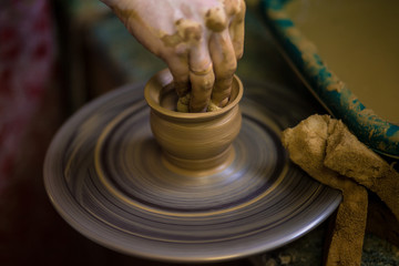 Close-up hands of potter in apron making vase from clay, selective focus. Making it together. Top view of potter teaching to make ceramic pot on pottery wheel