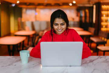 Young attractive Indian student working with a laptop and enjoying a coffee 