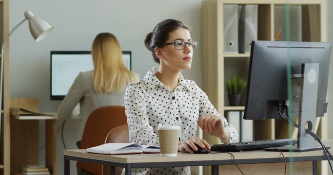 Caucasian beautiful woman sitting at the laptop computer in the office during workday, then her work being done ang going home with a smile. Indoor.