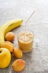 Apricots, Apple and banana and fruit smoothie in glass on patterned linen tablecloth.