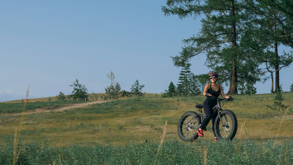 Obraz premium Fat bike also called fatbike or fat-tire bike in summer riding in the forest. Beautiful girl and her bicycle in the forest. She rolls her bike and poses to the operator.