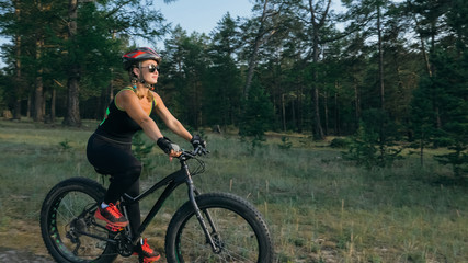 Fototapeta premium Fat bike also called fatbike or fat-tire bike in summer riding in the forest. Beautiful girl and her bicycle in the forest. She rolls her bike and poses to the operator.