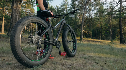 Fototapeta na wymiar Fat bike also called fatbike or fat-tire bike in summer riding in the forest. The woman rides a bicycle among trees and stumps. He overcomes some obstacles on a bumpy road.