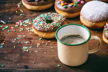 Coffee donuts and krepfen, sprinkles and powder sugar, many on wooden table background.