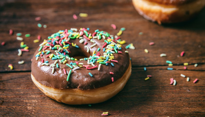 Donut chocolate glaze and sprinkles isolated, wooden table blurry background.