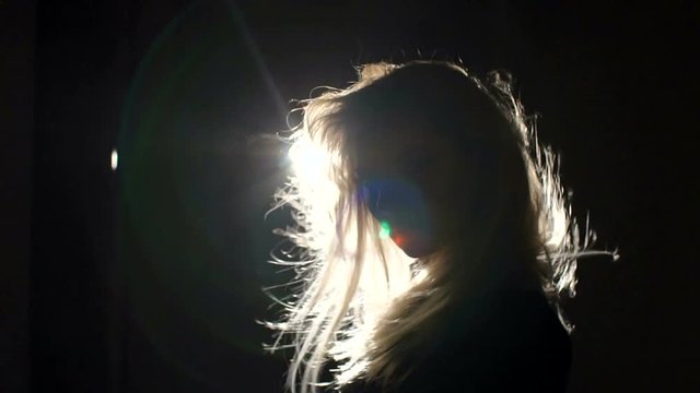 Close-up silhouette of a girl with long blond hair in the dark. Luxurious girl Waving her head and her hair flies in different directions in the dark with the light of a bright lantern, slow motion.
