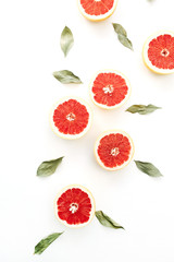 Red sliced grapefruits and green leaves on white background. Flat lay, top view food concept.
