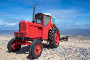 Naklejka premium Little old red diesel tractor on the beach.