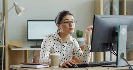 Young tired woman in glasses sitting at the laptop computer while working in the office, then almost falling asleep and waking up. Indoor. - Powered by Adobe