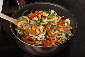 Stirring vegetables with mushrooms in a frying pan on a dark background. Cooking food