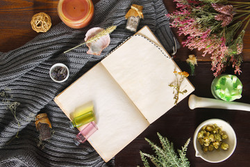 Fototapeta na wymiar An open empty vintage notebook surrounded by herbs, alchemy appliances, potions and ingredients lies on a dark wooden table. Magic alchemy and occultism. Flat lay with copy space for text. Mock up