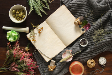 An open empty vintage notebook surrounded by herbs, alchemy appliances, potions and ingredients lies on a dark wooden table. Magic alchemy and occultism. Flat lay with copy space for text. Mock up