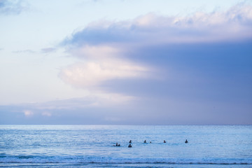 group of peaceful surfers sitting on the surf table waiting for some waves in a flat ocean tide and waves. beautiful sky with colored clouds, sunrise at the sea
