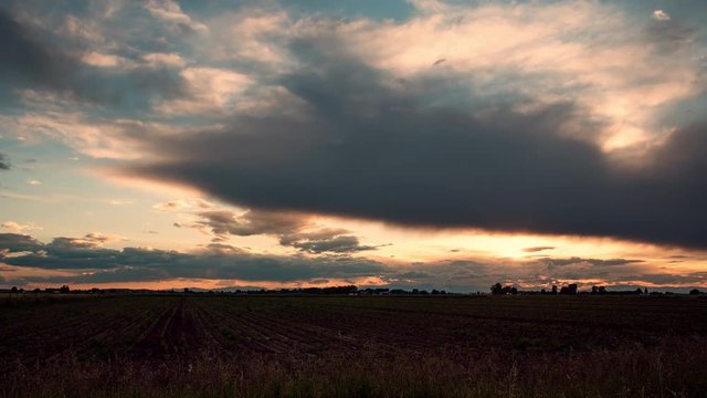 Time lapse of colorful sunset over farm field in Idaho as sun burst fades behind clouds