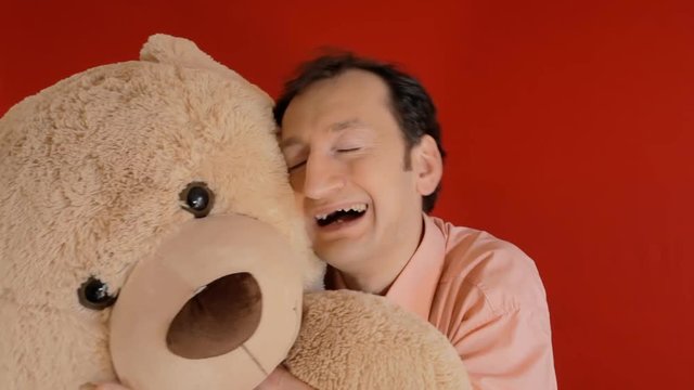 The friendship between a funny ugly man and a giant teddybear toy. Red background.
