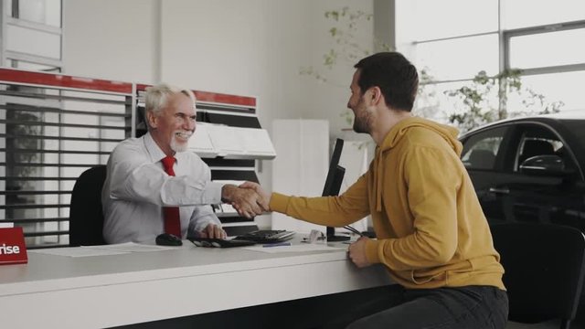 Very representive sales man an the car salon is giving the keys to the customer, at the desk.