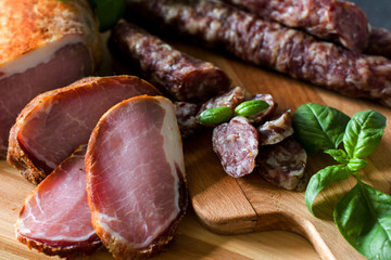 Dry home-made sausages and meat, serving slices on a wooden background decorated with a green basil on a gray background. Soft focus.