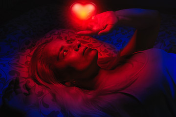 Concept of a woman laying in bed in the dark, illuminated with red light coming from the glowing...