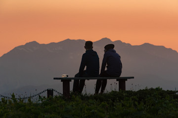 Fototapeta na wymiar Tourists rest on a bench in the mountains and admire the sunset over the mountain peaks.