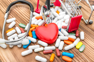 Shopping cart with pills with red heart and stethoscope on wooden background.  Medical background. Close up.