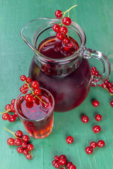 Red currant juice in glass and carafe with fruits on wood