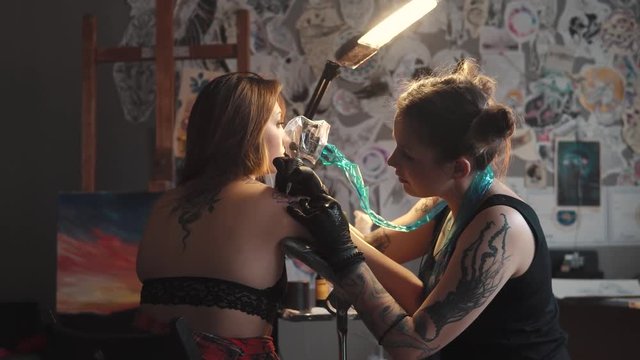 master tattoo is doing tattoo in a home studio. girl tattooist working tattoo machine in home studio. girl doing a tattoo on her shoulder
