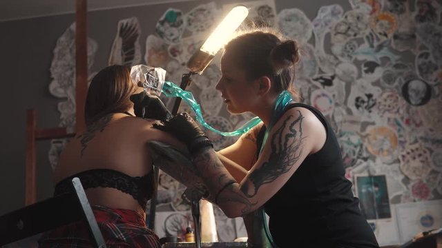 master tattoo is doing tattoo in a home studio. girl tattooist working tattoo machine in home studio. girl doing a tattoo on her shoulder