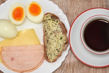 bread with butter and herbs, half boiled egg, tea and sausage with cheese on a white plate