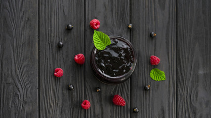 jam and raspberries and currants on a wooden background