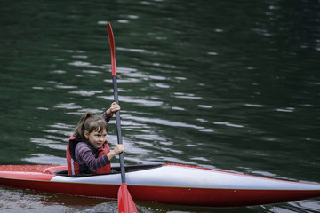 young teenager girl actively manages a sports kayak boat on a beautiful river.