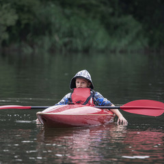 teenager boy in a tail boat kayak put his oar on the boat and tiredly dropped his hands into the river, drifting along the river.