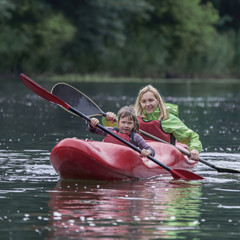 Mom and daughter fun and amicably manage a canoe boat on a wide river.