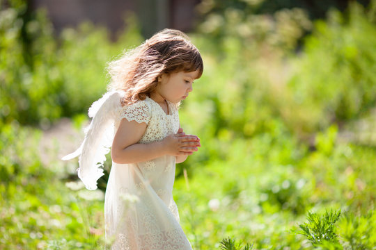 Beautiful little Angel girl standing at the forest with arms close to her chest as in prayer