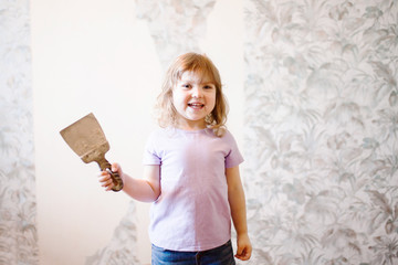 Adorable little girl repairing wall, holding putty knife