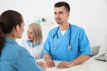 Young male doctor and senior female receptionist working with client in hospital