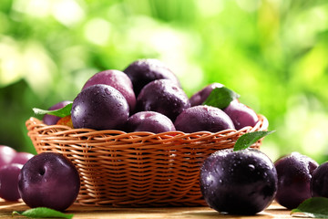 Wicker basket with ripe juicy plums on table