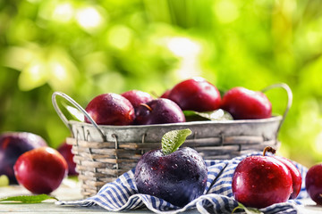 Basket with ripe juicy plums on table