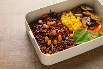Lunch box with tasty red rice and vegetables on table