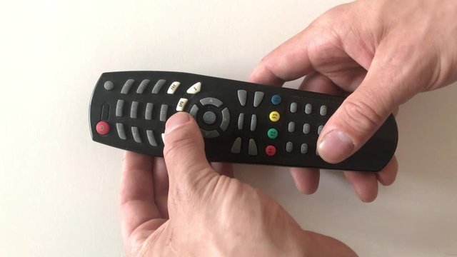 Hand holding tv remote and pushing exit button. White background.