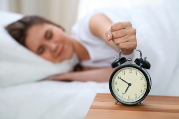 Sleepy young woman stretching hand to ringing alarm willing turn it off. Early wake up, not getting...