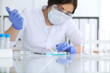 Close-up of professional female scientist in protective eyeglasses making experiment with reagents...