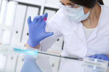 Close-up of professional female scientist in protective eyeglasses making experiment with reagents...
